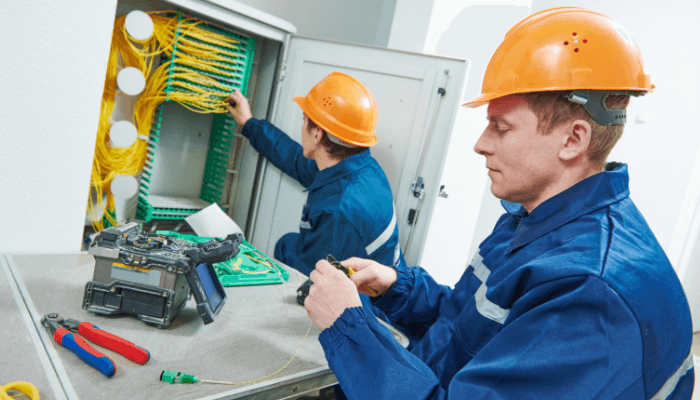 dos personas instalando fibra optica en un tablero y con uniforme